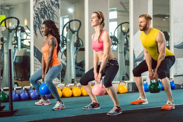 Three young people holding kettlebells during functional training — Stock Photo, Image