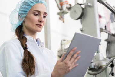 Tablet Pc hakkında bilgi çağdaş bir fabrikada iş sırasında analiz edilirken Beyaz önlük ve koruyucu şapkalar giyen kadın uzman