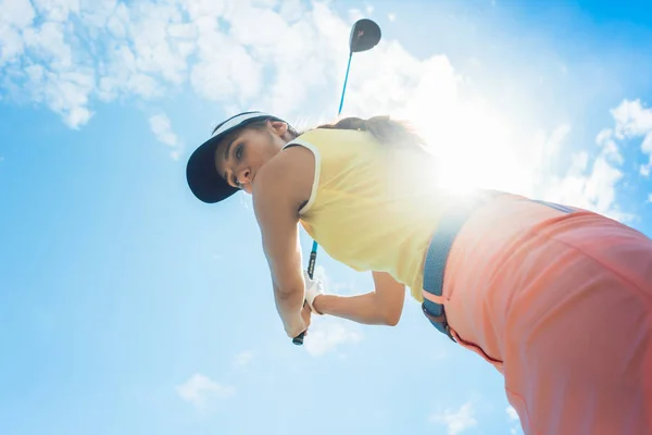 Low-angle view of a female professional player holding up the iron club with concentration for strike while playing golf outdoors against cloudy sky