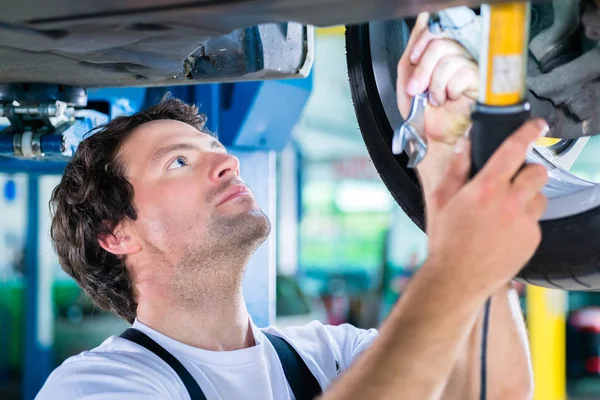 Mechanic working in car workshop on wheel — Stock Photo, Image