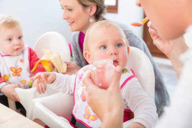 Annesine, besleyici meyve püresi yanında başka bir bebek evde yerken seyir mavi gözlü bir kız sevimli ve sağlıklı bebek portresi