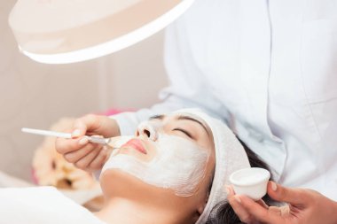 Uzman Yumuşak dokunuş altında rahatlatıcı, onun yanakları beyaz yüz maskesi efektleri gençleştirici ile uygulayarak genç bir kadın yüzü Close-Up