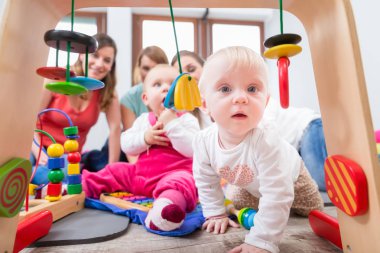 İlerleme ve merak çok renkli ahşap oyuncak, annesi ve bir aile dostu ile yerde otururken ulaşmaya tarafından gösterilen şirin bebek kız