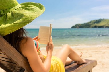 Sahilde ahşap şezlong üzerinde yaz tatili sırasında güneşli bir günde Flores Adası, Endonezya otururken bir kitap okuma güzel genç bir kadın yan görünüm
