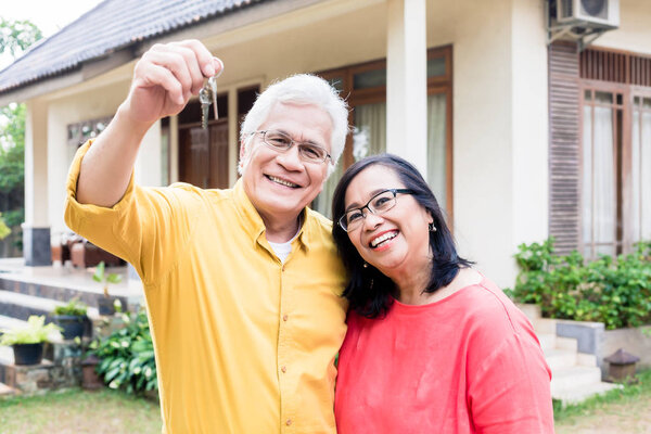 Portrait of a happy senior man posing with his wife while holding the keys of a residential house 