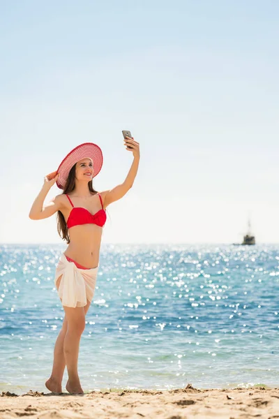 Красивая Молодая Женщина Модной Полосатой Шляпе Позирует Фотографии Селфи Пляже — стоковое фото
