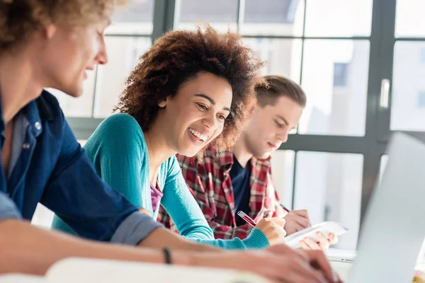 Cheerful Young Woman Writing Assignment While Sitting Desk Two Classmates — Stock Photo, Image