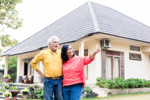 Happy elderly couple showing thumbs up in front of their new residential property