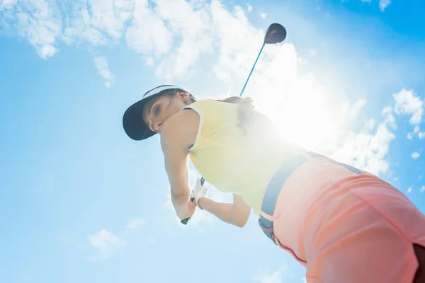 Low-angle view of a female professional player holding up the iron club with concentration for strike while playing golf outdoors against cloudy sky