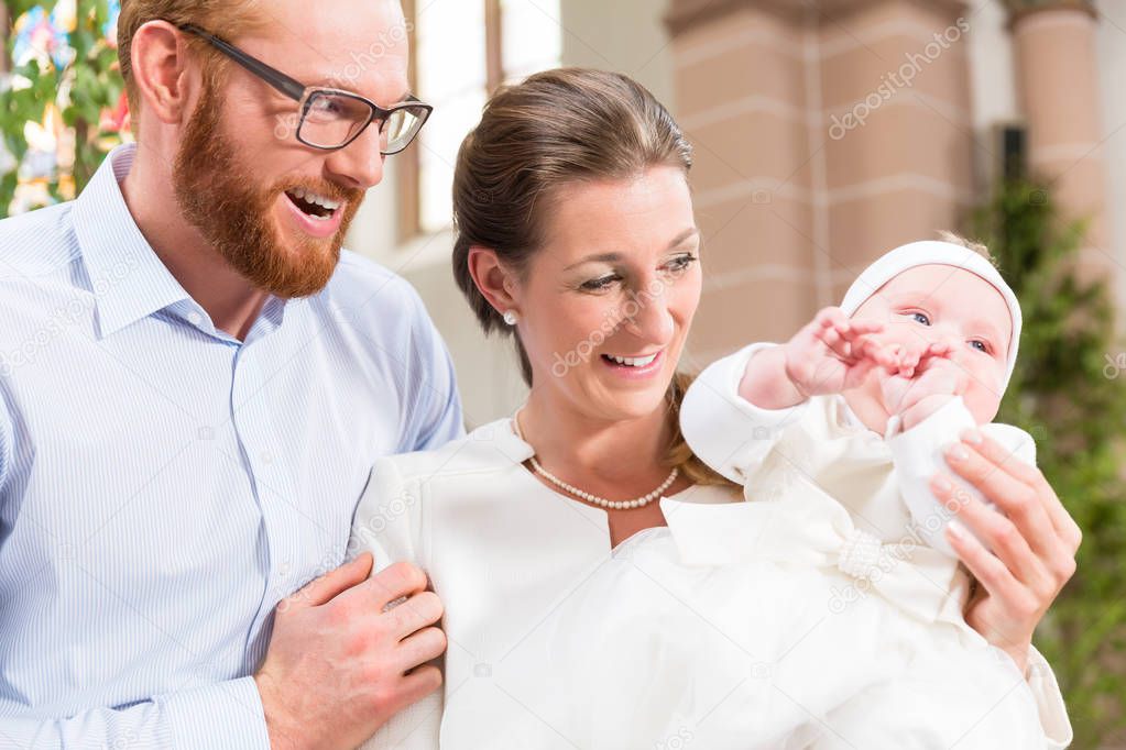Young parents at the church with their baby wearing a christening gown 