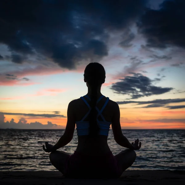 Mujer en forma sentada en posición de loto mientras practica yoga en la playa —  Fotos de Stock