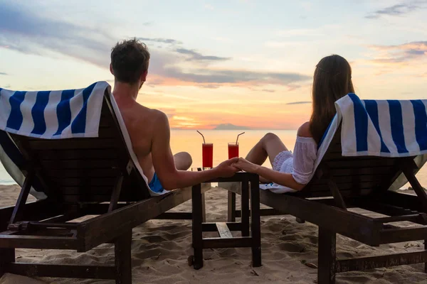 Młoda para picia koktajli na plaży o zachodzie słońca podczas wakacji — Zdjęcie stockowe