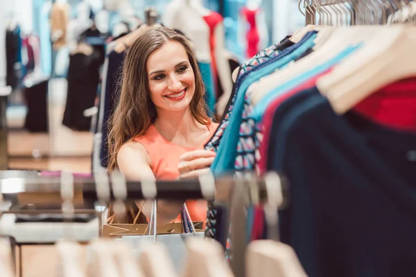 Kvinna som bläddrar klänningar på rack i modebutik — Stockfoto