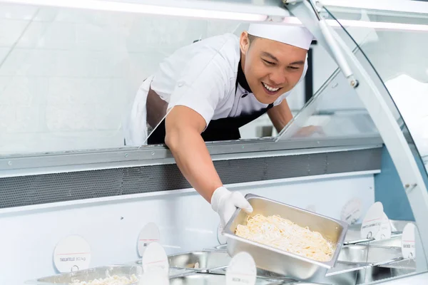 Sorrindo chef asiático enchendo um contador de exibição — Fotografia de Stock
