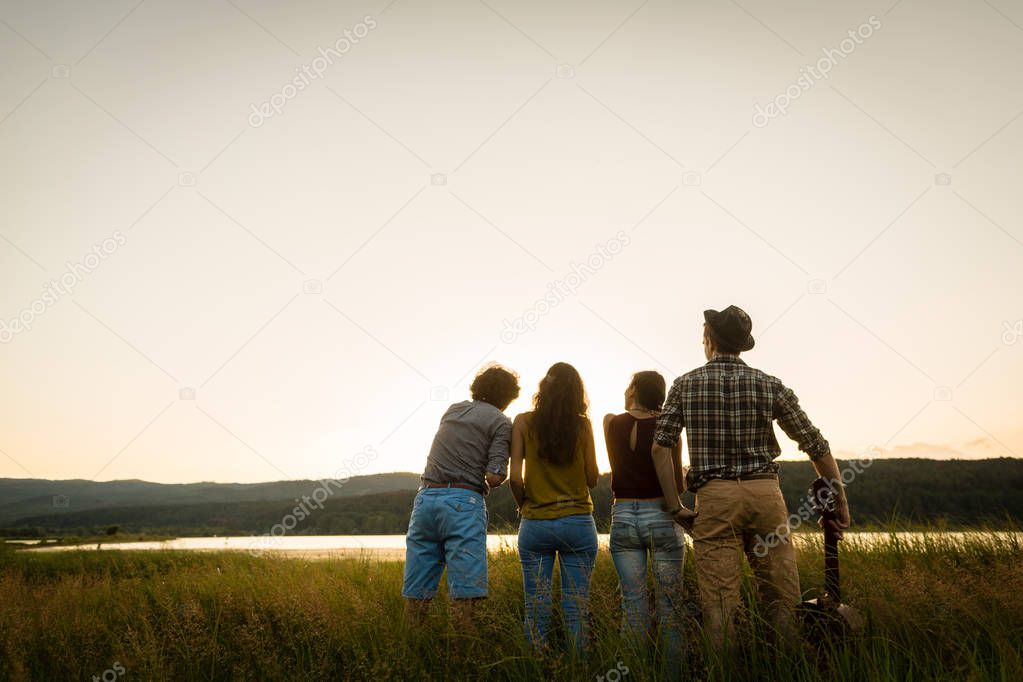 Group of friends in dusk of summer day looking to horizon