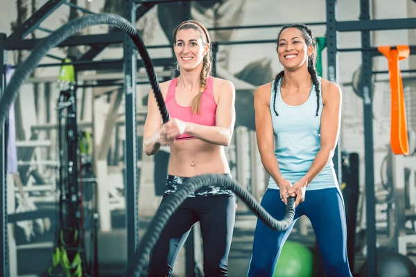 Two beautiful and strong women waving battle ropes during functional training — Stock Photo, Image