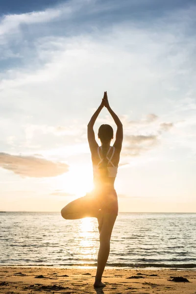 Silhouette di una donna che pratica la posa albero yoga su una spiaggia — Foto Stock