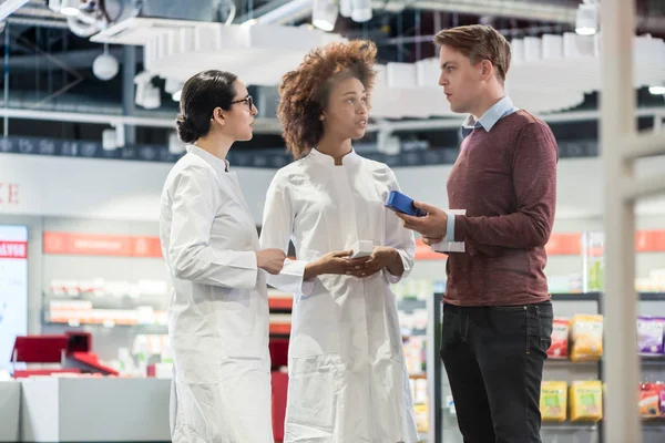 Jovem pedindo opinião aos farmacêuticos sobre prescrição — Fotografia de Stock