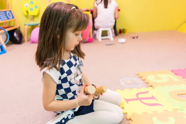 Симпатичная дошкольница смотрит на красочный коврик-головоломку — стоковое фото
