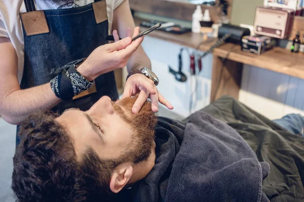 Bearded young man ready for shaving in the hair salon of a skilled barber — Stock Photo, Image