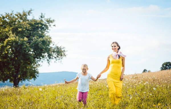 Mãe com sua filha correndo em um prado de verão — Fotografia de Stock