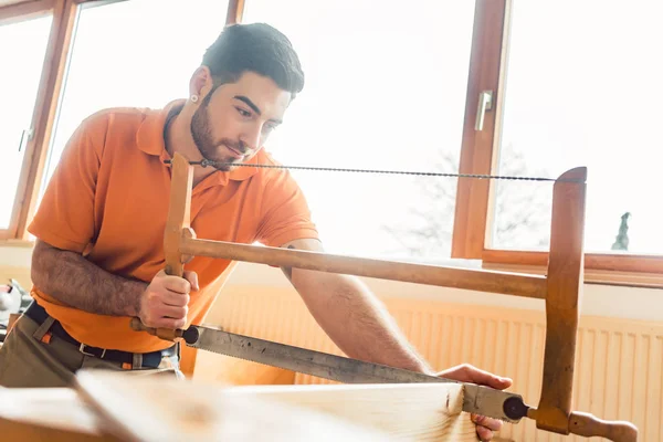 Carpintero joven trabajando en madera con sierra de marco — Foto de Stock