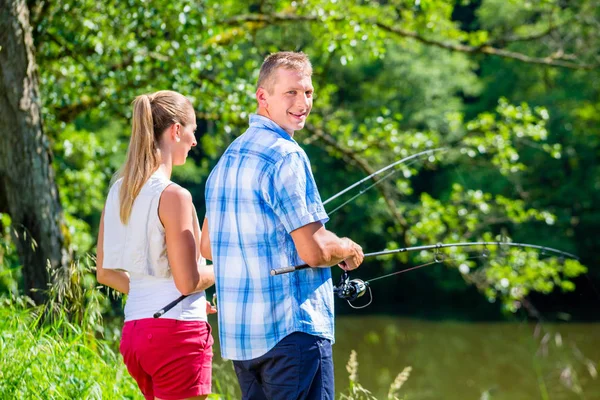 Giovane coppia pesca o pesca in piedi sulla riva del fiume — Foto Stock