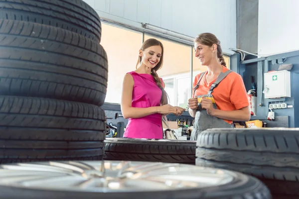 Mecânico de auto feminino útil verificando o número de identificação de um pneu — Fotografia de Stock
