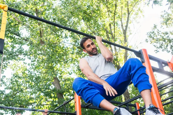 Poderoso joven haciendo flexiones de un brazo mientras cuelga en un bar en el parque — Foto de Stock