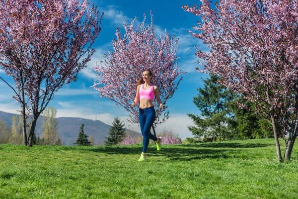 Mulher fazendo esporte correndo na colina entre árvores de cereja florescentes — Fotografia de Stock