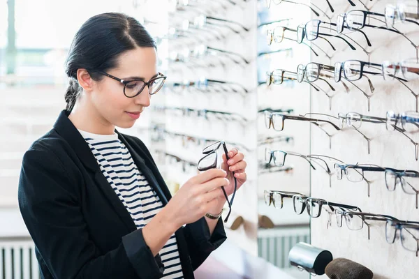 Vrouw nemen van glazen plank in opticien shop — Stockfoto