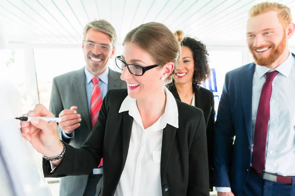 Zakenvrouw schrijft op een flipboard voor drie collega 's — Stockfoto