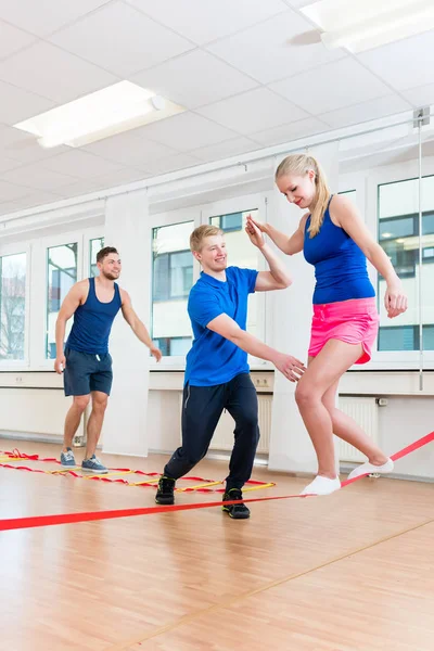 Physio praticando slacklining com atletas no ginásio — Fotografia de Stock