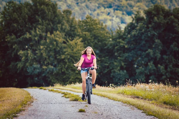 Chica en bicicleta en bicicleta por un camino de tierra en verano — Foto de Stock