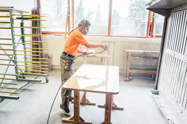 Mulher carpinteiro verniz pulverização em uma mesa em que ela trabalha — Fotografia de Stock