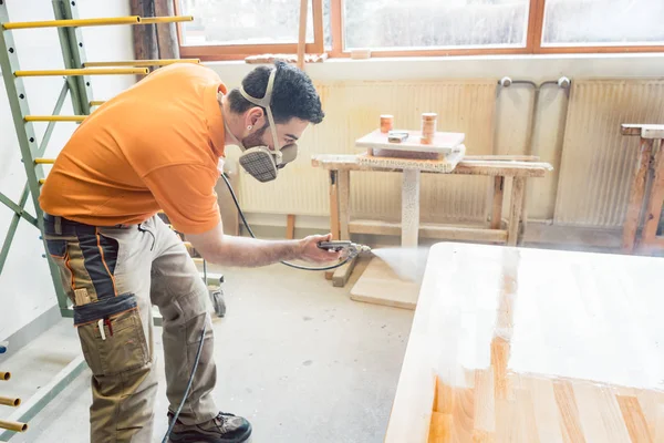 Tischler sprüht Lack auf einen Tisch, an dem er arbeitet — Stockfoto