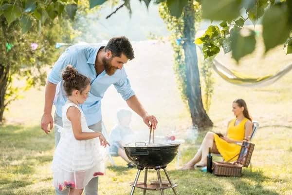 Meisje kijken vader voorbereiding van vlees op de grill barbecue tijdens familie picknick — Stockfoto