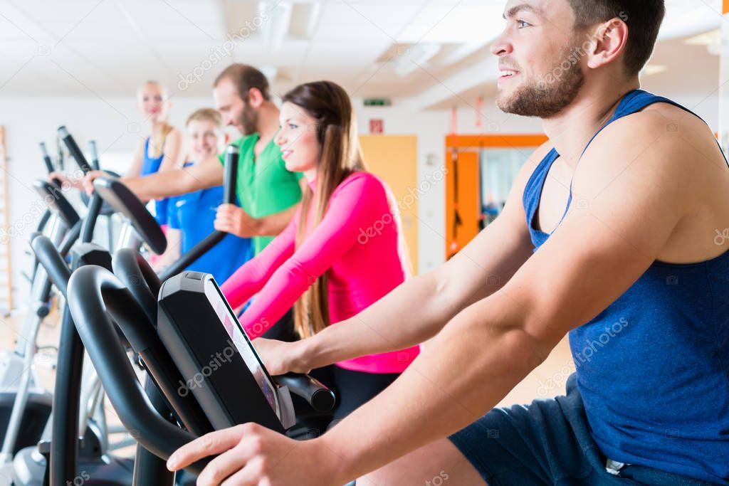 Men and women on cardio bikes in gym 