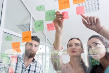 Anımsatıcılar bir ofis, bir modern ortak çalışma alanı içinde kendi meslektaşı yanındaki şeffaf duvar ilanıyla güvenilir genç işçilerin düşük açılı görünüş
