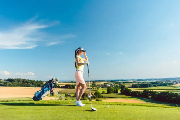 夏の晴れた日に田舎のゴルフ場の緑の草の地平線を見ながらモダンなゴルフの服装を身に着けているフィット女性の側面図 — ストック写真