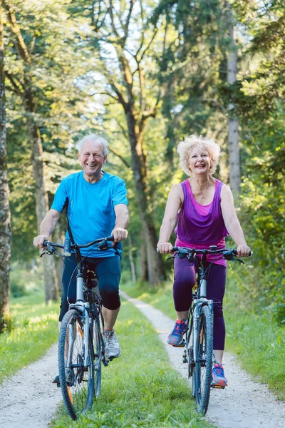 Happy and active senior couple riding bicycles outdoors — Stock Photo, Image