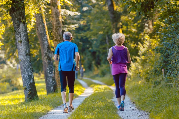 Vista posteriore a tutta lunghezza di una coppia di anziani che fanno jogging insieme all'aperto — Foto Stock