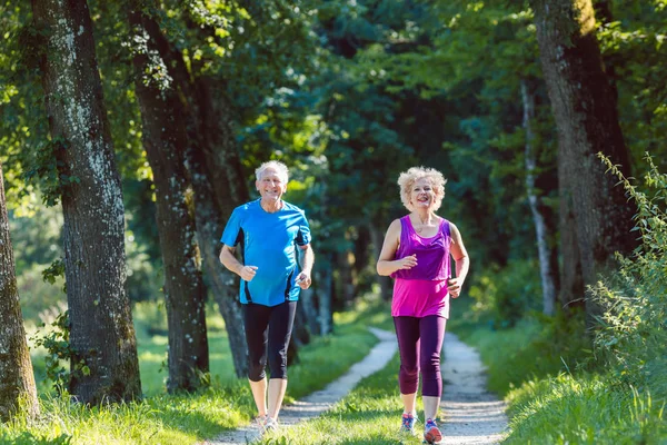 Два активных пенсионера со здоровым образом жизни улыбаются во время пробежки — стоковое фото