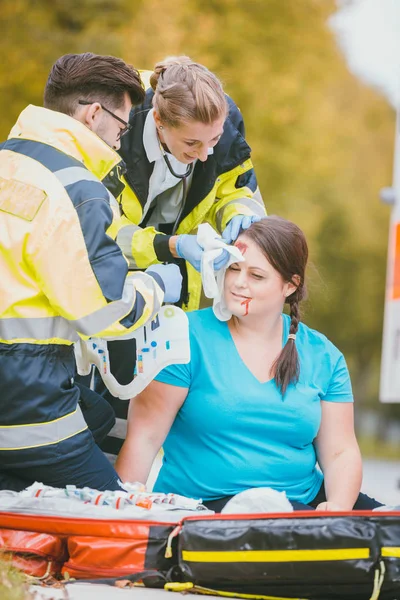 Медики скорой помощи перевяжут рану головы раненой женщины — стоковое фото