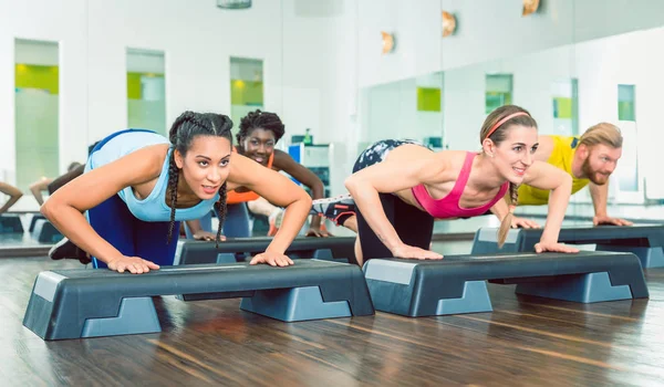 Mujeres decididas ejercitando flexiones en plataforma escalonada aeróbica —  Fotos de Stock