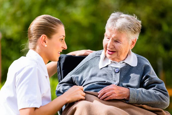 Zdravotní sestra držel ruku s starší žena na vozíku — Stock fotografie