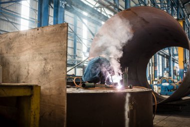 Mavi yakalı işçi bir fabrikanın içinde kaynak yapıyor.