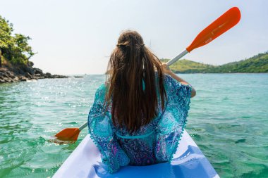 Genç kadın bir pastoral ada ve kıyı bir kano kürek çekmeye