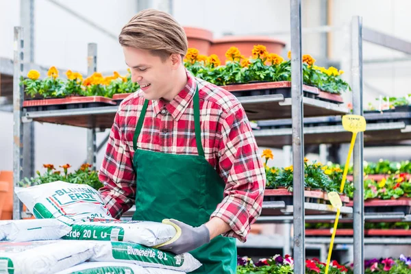 Ung man bära en påse krukväxtjord under arbete på blomstermarknaden — Stockfoto