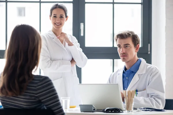 Junge Krankenschwester hört einem erfahrenen Arzt zu, während sie einen Patienten konsultiert — Stockfoto